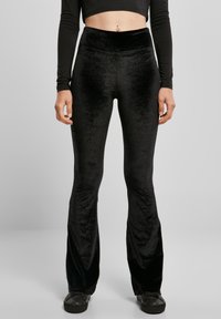 Musta samettiset liehupöksyt korkean vyötärönauhalla, joissa on pehmeä rakenne ja sileä pinta. Yhdistetty pitkähihaiseen lyhytpaitaan ja mustiin kenkiin.