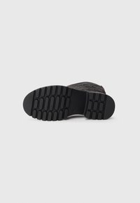 Black rubber boot sole with textured tread pattern, featuring ridges and grooves for grip and stability. No visible logos or accents.