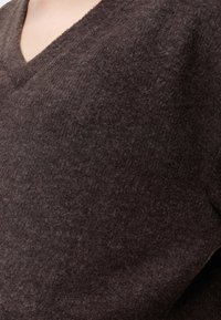 Gros plan sur un tissu en laine doux de couleur marron foncé sur un pull à col en V porté par une personne à la peau claire.