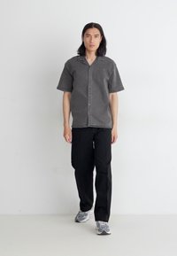 Short-sleeve, button-up shirt in dark gray with a soft texture, paired with loose black pants and gray sneakers. Simple design, no patterns.