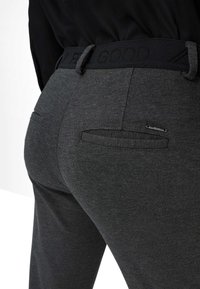 Graue Hose mit strukturiertem Obermaterial, ausgestattet mit einem schwarzen elastischen Bund, der mit "FEEL GOOD" beschriftet ist, sowie einer Gesäßtasche mit einem Reißverschluss.