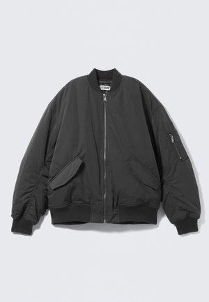 Veste bomber noire avec fermeture éclair frontale, deux poches à rabat, poignets et ourlet côtelés, et poche zippée sur la manche gauche.