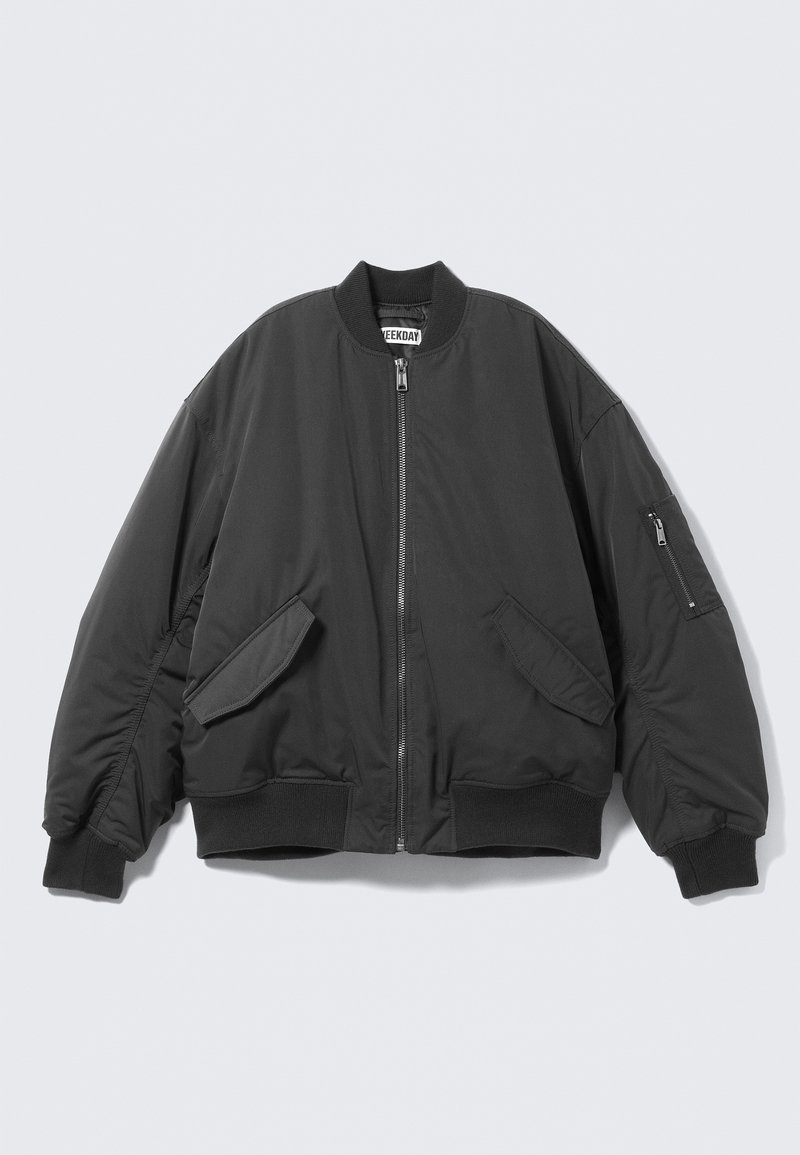 Veste bomber noire avec fermeture éclair frontale, deux poches à rabat, poignets et ourlet côtelés, et poche zippée sur la manche gauche.