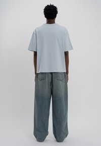 Ανοιχτό μπλε, φαρδύ βαμβακερό t-shirt με κοντά μανίκια, συνδυασμένο με φαρδιά παντελόνια τζιν σε ξεθωριασμένο μπλε χρώμα με κλασικό σχέδιο πίσω τσέπης.