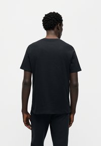 Μαύρο βαμβακερό t-shirt με κοντά μανίκια, διαθέτει στρογγυλή λαιμόκοψη και άνετη εφαρμογή. Απλός σχεδιασμός χωρίς εμφανή λογότυπα ή σχέδια.