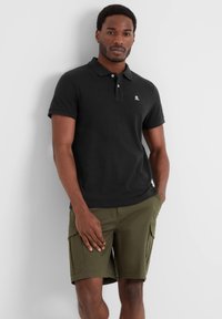 Black polo shirt with short sleeves, featuring a logo on the left chest, paired with olive green cargo shorts with side pockets.