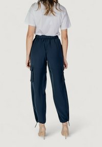 Pantaloni cargo blu navy con cintura elasticizzata, dotati di tasche laterali e gambe affusolate, accompagnati da una maglietta bianca a maniche corte.