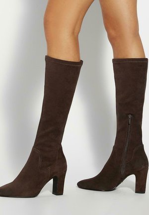 Bottes hautes jusqu'au genou en daim marron avec un bout pointu, un talon bloc et un détail de fermeture éclair latérale. Texture lisse avec des accents cousus le long des coutures.