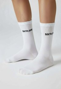 Weiße Baumwoll-Socken mit Rippenstruktur und schwarzem "SIXTH JUNE"-Logo an der Seite. Glatte Oberfläche und Standardzehen-Design.