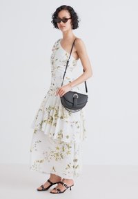 Vestido blanco floral con escote asimétrico y volantes en capas, combinado con un pequeño bolso cruzado negro y sandalias negras.