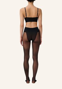 Bralette nera con spalline sottili e un paio abbinato di collant neri trasparenti con design a taglio sul retro, che offre una texture liscia.