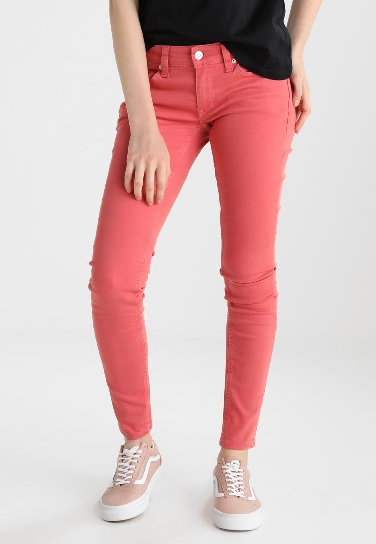 Jeans de mezclilla rosa de corte ajustado con una cintura de altura media, costuras en contraste, cinco bolsillos y detalles de hardware metálico. Combinados con zapatillas rosas.