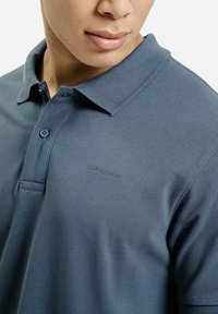 Granatowa koszulka polo z teksturowanej tkaniny, klasycznym kołnierzykiem i pojedynczym zapięciem na guzik. Dyskretne logo na klatce piersiowej.