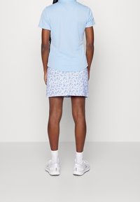 Light blue short-sleeve polo shirt paired with a patterned blue and white skirt. White athletic shoes and socks. Visible back view.