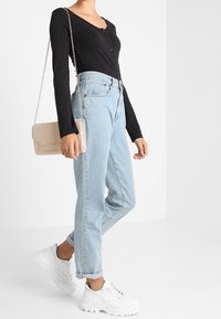 Maglietta nera a maniche lunghe con bottoni, jeans a vita alta di colore azzurro chiaro, sneakers bianche chunky e una borsa a tracolla beige con catena.