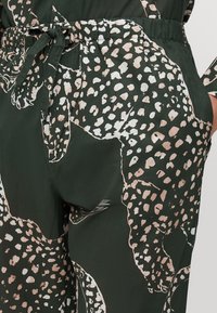 Tissu vert foncé avec de grands motifs tachetés en beige et blanc, doté d'une taille élastique et d'un détail à nouer pour un ajustement réglable.