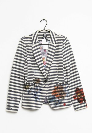 Černobíle pruhovaný blazer s květinovým vzorem a ručně psaným textem, s jedním knoflíkem a zářezovými klopami, zavěšený na černém ramínku.