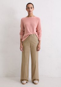 Lichtroze geribbeld truitje met brede mouwen, gecombineerd met high-waisted beige wijde broek en plateau sneakers met een witte basis.