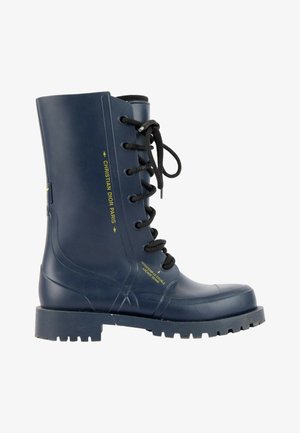 Botte de combat en caoutchouc bleu marine avec lacets noirs, semelle épaisse et texte "Christian Dior Paris" en jaune sur le côté.