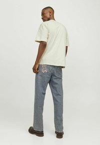 Light beige cotton t-shirt with short sleeves, paired with blue denim jeans featuring pink embroidered design on back pocket.