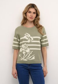 Kortærmet olivengrøn sweater med cremede vandrette striber og blomstermotiv. Strikket tekstur, rund halsudskærning, afslappet pasform. Blå denim jeans iført.