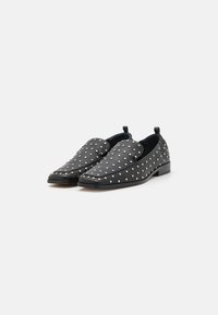 Black leather slip-on shoes with a flat heel, featuring a dotted pattern of silver studs across the upper. Smooth texture with a sleek design.