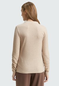 Beige top met lange mouwen, een ronde hals, een losse pasvorm en geplooide details op de mouwen, gemaakt van een zachte, gestructureerde stof.