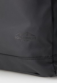 Sac à dos noir en tissu texturé avec une surface lisse. Présente un logo en relief "SOUTHWEST BOUND" et un graphique de montagne courbée sur un côté.