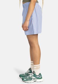 Blue shorts with red vertical stripes, elastic waistband, two side pockets; paired with green athletic shoes and white striped socks.