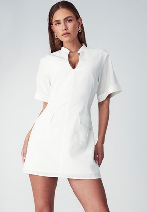 Vestido blanco de manga corta con cuello y escote en forma de llave. Presenta dos bolsillos frontales y un diseño ajustado, confeccionado en una tela texturizada.