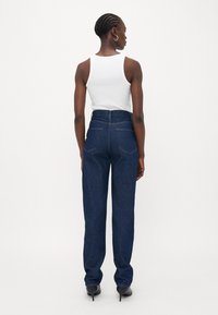 Hoge taille donkerblauwe denim jeans met een rechte pijp, achterzakken en een soepele textuur, gecombineerd met een witte tanktop.