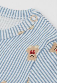 Modrá a bílá pruhovaná látka s potiskem medvídků s červenými mašlemi. Obsahuje dřevěný cvok detail poblíž výstřihu.