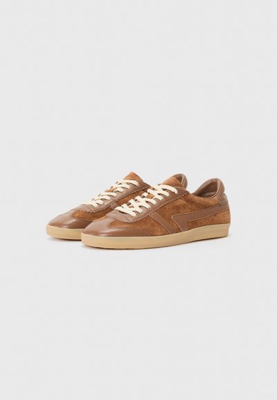 Bruna sneakers i läder och mocka, med låg profil, strukturerade detaljer och krämfärgade snören på en beige gummisula.