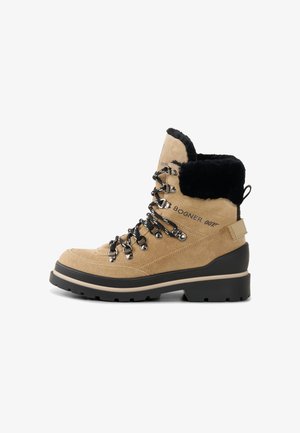Světle hnědé semišové turistické boty s černým umělým kožešinovým límcem, stříbrným kováním a černými tkaničkami. Silná černá gumová podešev s béžovým středovým detailem.