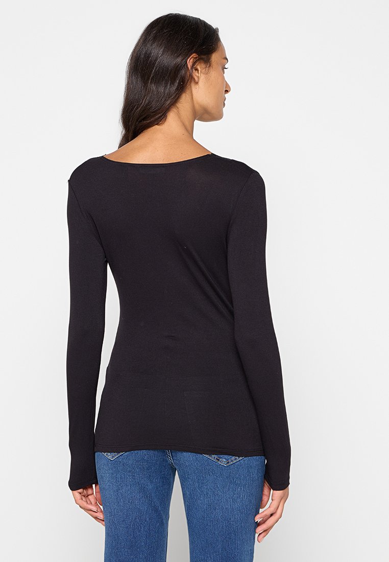 Top nero a maniche lunghe con scollatura a barca, silhouette aderente, tessuto morbido e orlo dritto. Abbinato a un paio di jeans blu.