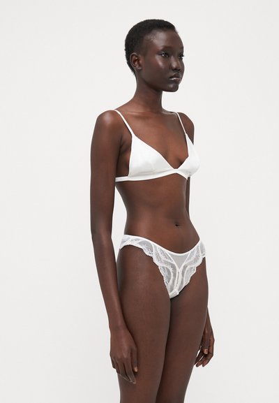 Bralette triangolare in satin bianco con spalline sottili e coordinato con perizoma in pizzo bianco con bordi scallop e motivo floreale.