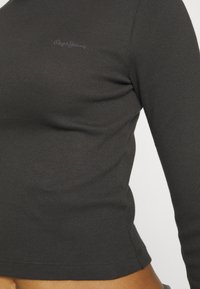 Sötétszürke bordázott hosszúujjú felső, testhez simuló kialakítással. Diszkrét logó részlet a mellkason, kerek nyakú és sima textúrájú.