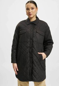 Svart quilted lang kappe med to frontlommer, knappelukking og krage. Har et diamantmønster og en avslappet passform.