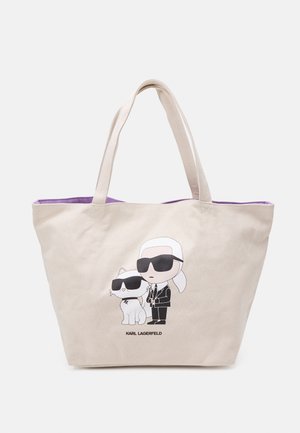 Bolso tote beige con interior morado, con un dibujo de caricatura de Karl Lagerfeld con gafas de sol, de pie junto a un gato que también lleva gafas de sol.