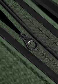 Gros plan d’un tissu texturé vert foncé avec une fermeture éclair noire partiellement ouverte et un curseur noir sur un sac ou une housse.