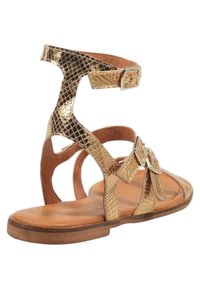 Sandalias de cuero doradas con textura de reptil, que cuentan con múltiples correas y dos hebillas ajustables, sobre una suela de madera plana.