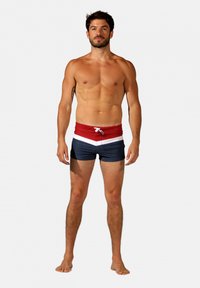 Shorts de bain rouges et bleus marine avec des rayures blanches horizontales ; taille à cordon de serrage ajustable, longueur de jambe moyenne et texture lisse.