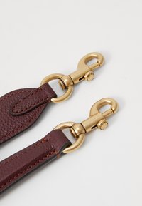 Burgundy leather strap with two gold-tone clasps. Textured surface, reinforced stitching, and polished hardware accents.