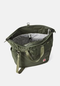 Sac fourre-tout vert olive avec une ouverture zippée, en tissu durable, bandoulière réglable et un intérieur spacieux gris. Présente un patch logo.
