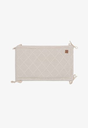 Coussin rectangulaire en tissu tricot beige clair, ornée d'un motif en losange et avec des extrémités nouées. Comprend une petite étiquette en cuir sur le côté.