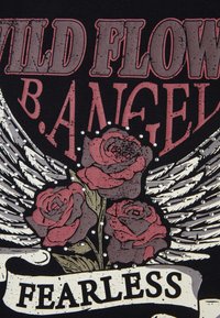 Camiseta gráfica negra con rosas rojas y grises, alas y la palabra "SIN MIEDO" en una pancarta, adornada con tachuelas plateadas.
