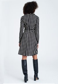 Abito a pois bianco e nero con maniche lunghe, vita aderente e gonna svasata; abbinato a stivali neri con tacco al ginocchio.