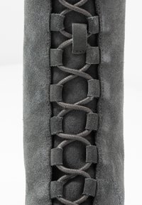 Stivale in suede grigio con finitura texturizzata, caratterizzato da dettagli a trama intrecciata, anelli in pelle e una superficie liscia lungo il lato.