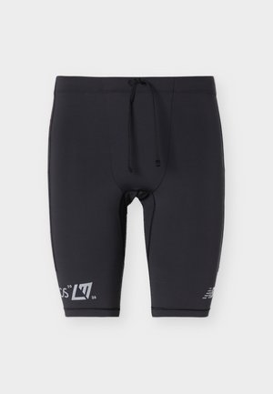Pantalones cortos atléticos negros ajustados con cinturilla de cordón y pequeños logotipos blancos en la parte baja de las piernas sobre un fondo liso.