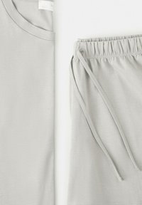 Grå kortærmet skjorte og matchende bukser med elastik i taljen og snøre, foldet fladt på en hvid baggrund.